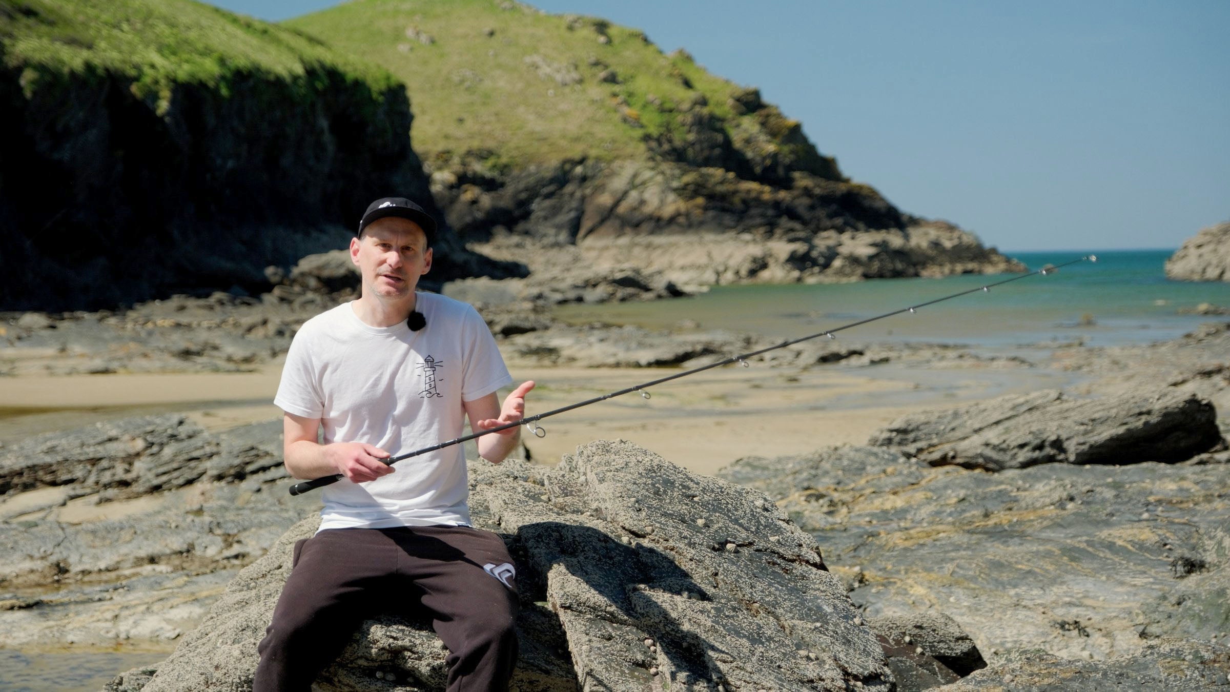 Ben Field talking through a rod on the rocks, back to the sea